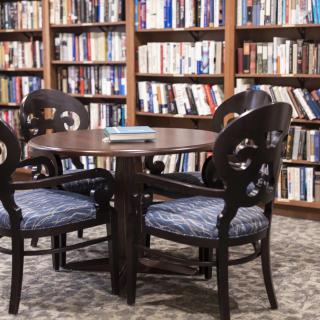 A cozy reading area with a round table and chairs surrounded by shelves filled with books.