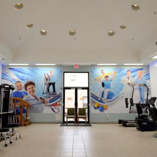 A spacious interior of a rehabilitation gym featuring exercise equipment and a vibrant mural.
