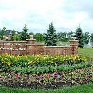 A scenic view featuring a brick sign surrounded by vibrant flowers and lush greenery in a park setting.