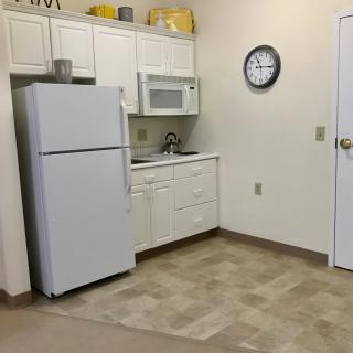A small kitchen with a refrigerator, microwave, sink, and clock on the wall.