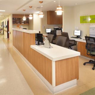 A modern hospital reception area with desks, computers, and office chairs in a well-lit hallway.