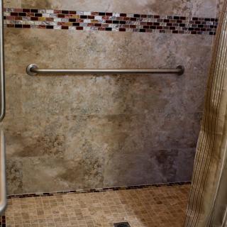 A tiled shower with a grab bar and decorative mosaic trim.