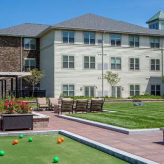 A sunny outdoor area featuring a bocce court, patio furniture, and a large building.