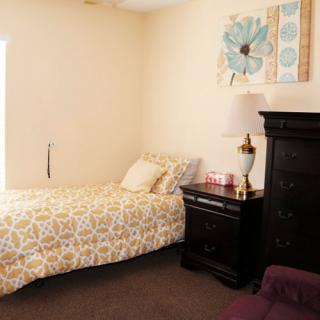 A cozy bedroom with a decorated single bed, nightstand, lamp, and artwork on the wall.