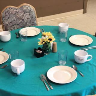 A neatly arranged dining table featuring a turquoise tablecloth, plates, cups, and a floral centerpiece.