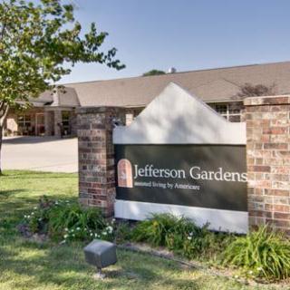 Entrance sign for Jefferson Gardens with a background view of the building and greenery.