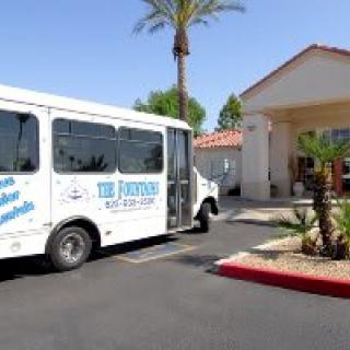 A white shuttle bus parked in front of a building with palm trees and a parking lot.