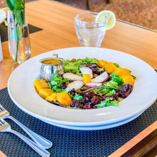 A colorful and fresh salad served at a restaurant, garnished with vibrant vegetables and dressing on the side.