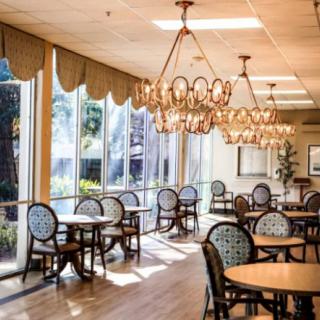 A well-lit cafe with elegant chandeliers and large windows, featuring round tables and patterned chairs.