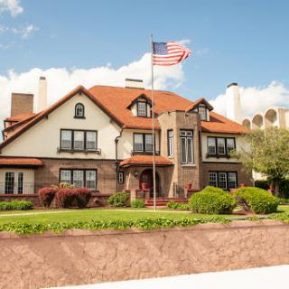 A beautifully designed residential house featuring traditional architecture, adorned with an American flag against a clear blue sky.