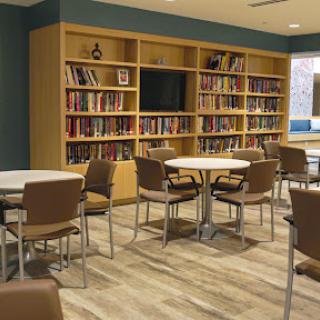 A cozy reading area featuring bookshelves filled with books, accompanied by tables and chairs for visitors.