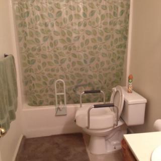 Accessible bathroom with handrails around the toilet and a green patterned shower curtain.