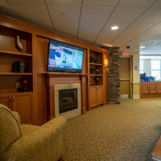 A cozy living room with a television mounted above a fireplace, surrounded by wooden shelves and comfortable seating.