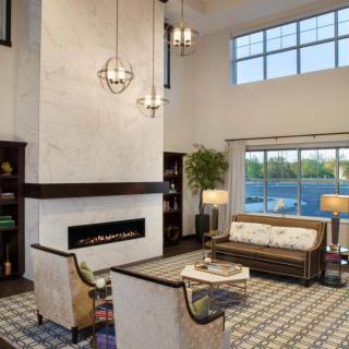 A modern living room with a high ceiling, featuring contemporary furniture, a fireplace, and a large window.