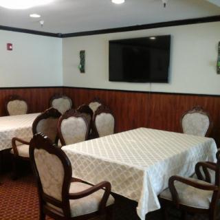 A dining room with two tables covered in white tablecloths, surrounded by upholstered chairs, and a television mounted on the wall.
