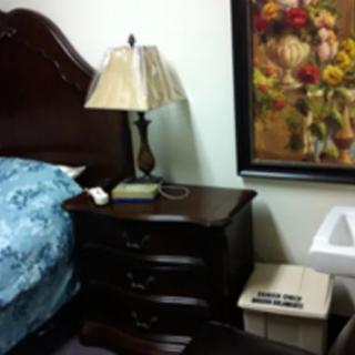 A cozy bedroom corner with a lamp on the nightstand and a floral painting on the wall.
