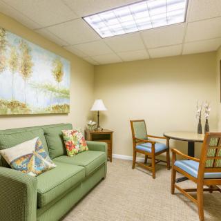 A cozy waiting room with a green sofa, chairs, and decorative artwork.