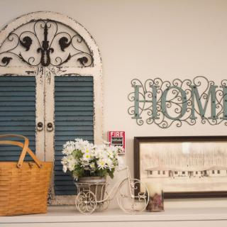A cozy home setup featuring vintage-style decorations, including a wicker basket, flowers in a decorative cart, and wall art that spells 'HOME'.
