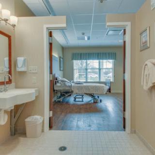 A view of a hospital patient room featuring a bed, window, and bathroom area.