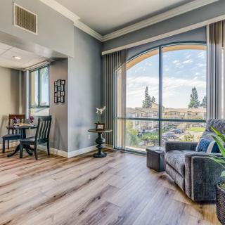 A cozy living room with a large window, featuring an armchair and wooden flooring that enhances the natural light.