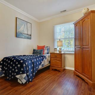 A cozy bedroom with a nautical-themed single bed, wooden wardrobe, and nightstand next to a window.