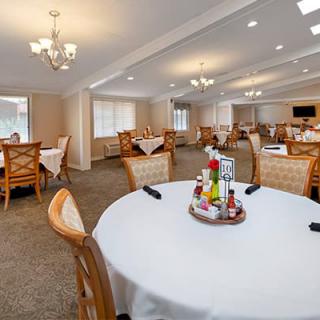 A spacious dining room with neatly arranged tables and chairs, featuring elegant chandeliers and large windows.