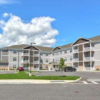 A modern residential apartment complex with a spacious parking lot under a clear, blue sky.
