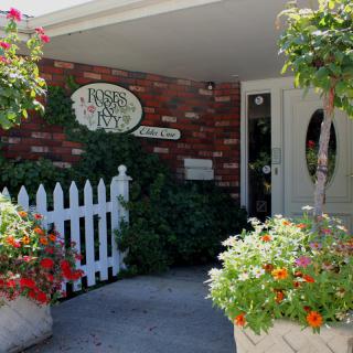 A welcoming entrance to a building with a brick exterior, adorned with colorful flowers and a white picket fence.