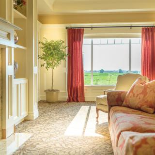 A cozy living room with a view of the landscape through a large window, featuring a sofa, curtains, and indoor plant.