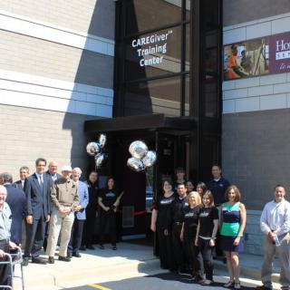 A group of people gathered for a ribbon-cutting ceremony outside a theater or similar venue.