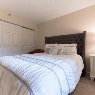 A cozy bedroom with a neatly made bed, featuring a tufted headboard and soft lighting from a bedside lamp.
