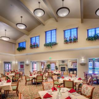 A spacious and elegantly decorated dining room with neatly arranged tables and chairs, illuminated by overhead chandeliers.