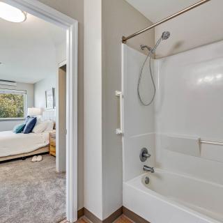 A bathroom with a bathtub and shower next to a bright and cozy bedroom.