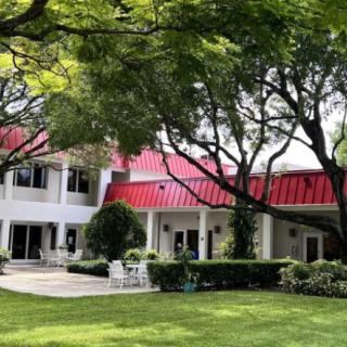 A beautiful house with a red metal roof surrounded by a lush garden and tall trees.