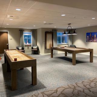A cozy game room featuring a shuffleboard and billiards table, illuminated by warm lighting.