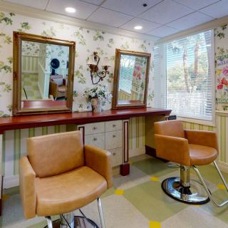 A cozy salon interior featuring two tan salon chairs with mirrors on the wall and floral wallpaper.