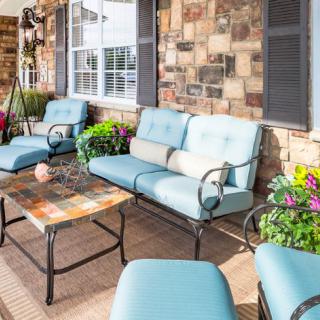 A cozy outdoor patio with cushioned seating and a coffee table, surrounded by decorative plants.