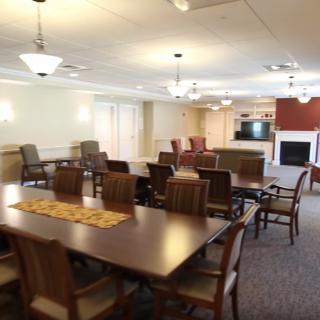A spacious interior dining area featuring several tables and chairs, with a kitchen and fireplace in the background.