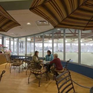 A cozy cafe with three people engaged in conversation by large windows during the day.