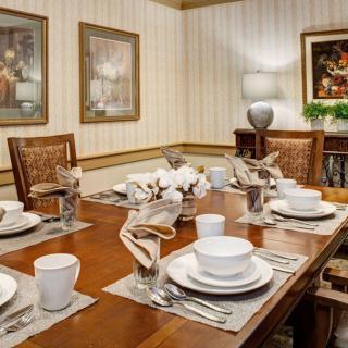 A warmly lit dining room with a neatly arranged table setting, featuring elegant dishware and decorative artwork on the walls.