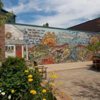 A vibrant mural decorates an outdoor garden area, surrounded by colorful flowers under a clear sky.