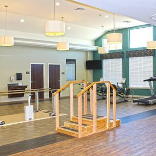 A spacious gym interior featuring exercise equipment, a wooden staircase, and mirrors.