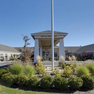 A building entrance with a landscaped area and a flagpole under a clear blue sky.