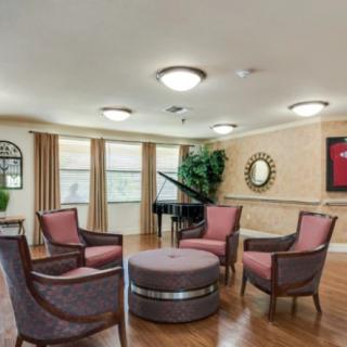 A cozy living room featuring a circle of elegant chairs around a central ottoman, with a grand piano in the background.