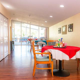A bright and welcoming dining area with a red tablecloth, wooden chairs, and natural light streaming in through large windows.