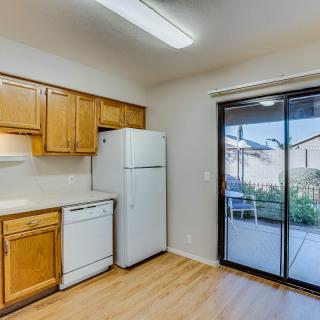 A brightly lit kitchen with wooden cabinets, a refrigerator, dishwasher, and a sliding glass door leading outside.