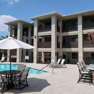 A modern apartment complex with an outdoor swimming pool and patio furniture under a sunny sky.