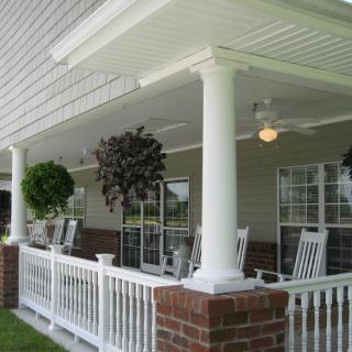 A cozy porch with white columns, rocking chairs, and hanging plants.