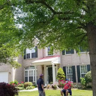 Two people conversing in front of a suburban house on a sunny day.