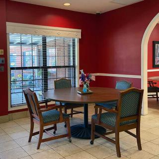 A cozy dining area with a round table and four chairs against red-painted walls, illuminated by natural light from a large window.